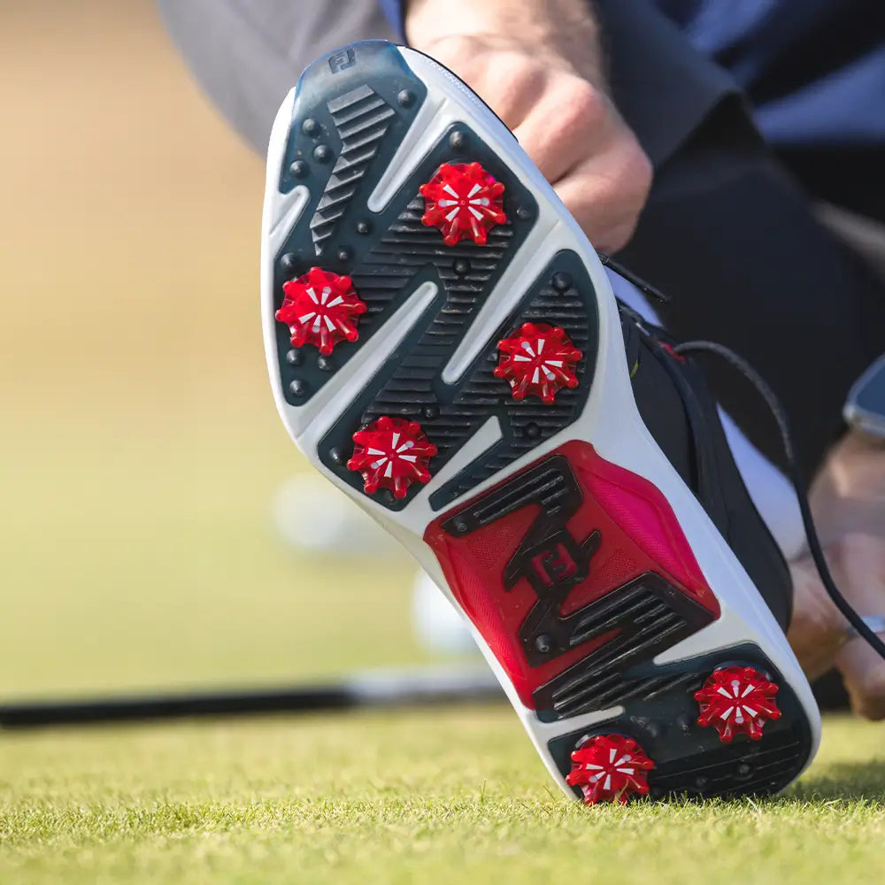 A bottom of a persons golf shoe showing the red pulsar golf spikes attached.