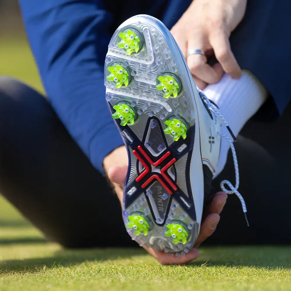 A person adjusting their golf shoe showing the green pivix golf spikes attached.