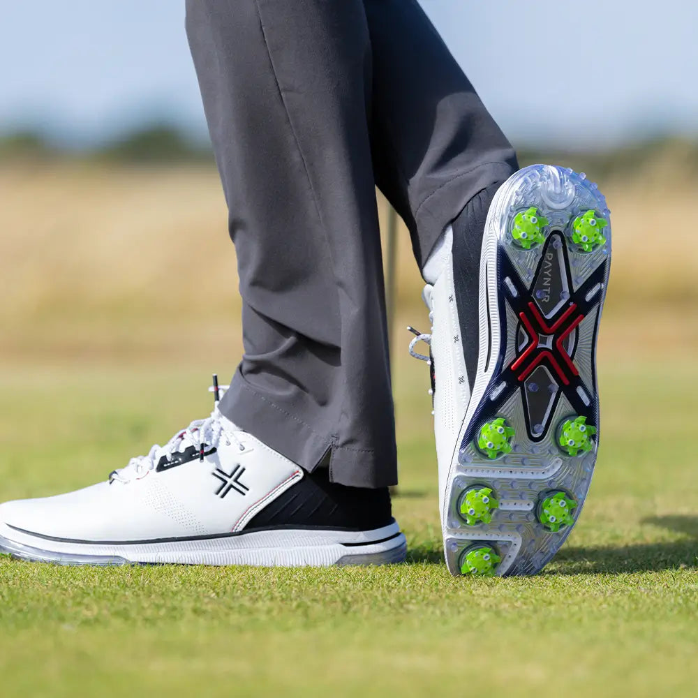 The underside of a persons golf shoe showing the green pivix golf spikes attached.