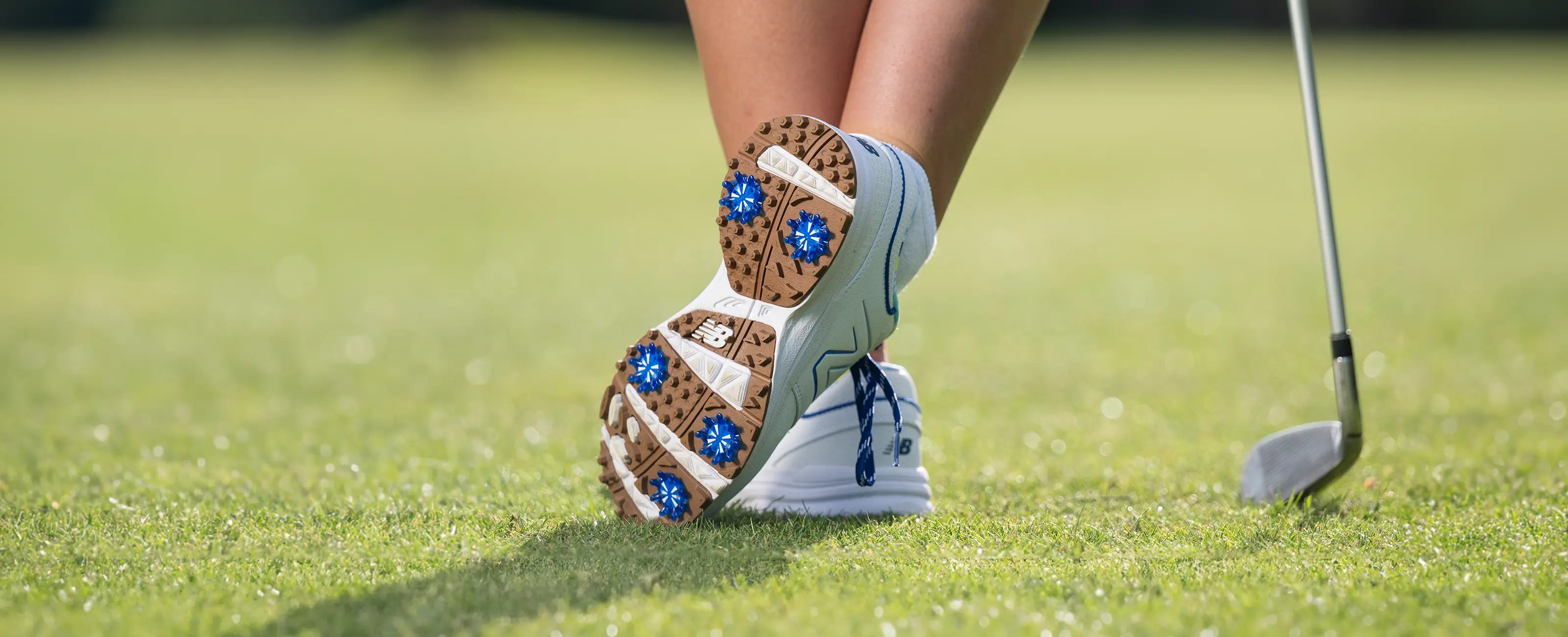 A person wearing azue blue Pulsar golf spikes on their new balance golf shoe.