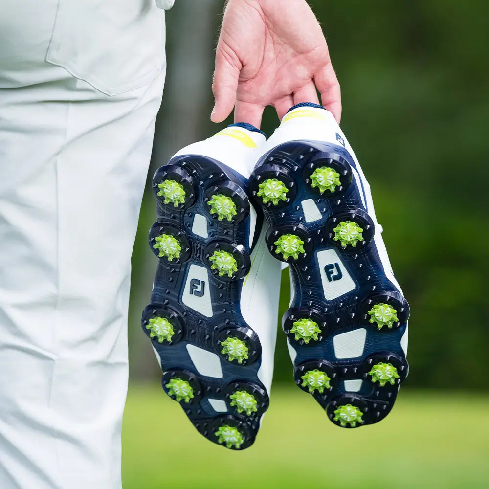 A golfer holding his shoes showing the underside attached slime green Pulsar Golf Spikes. 