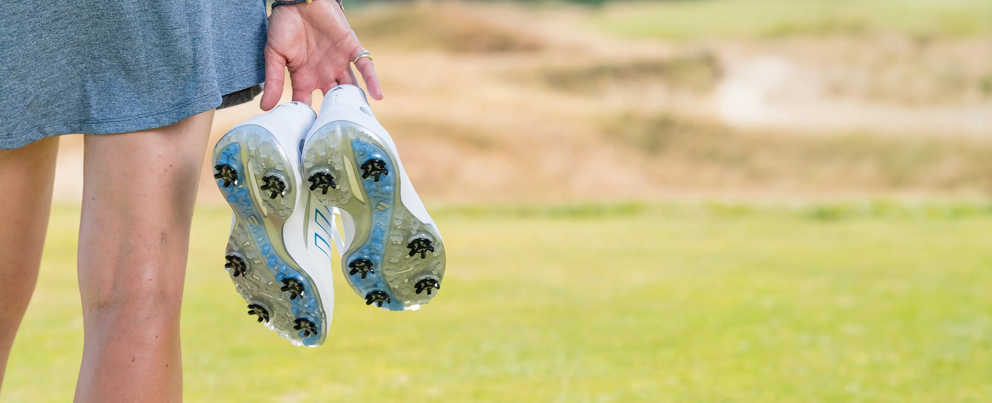 A woman holding a pair of golf shoes with Stealth spikes attached to them. 