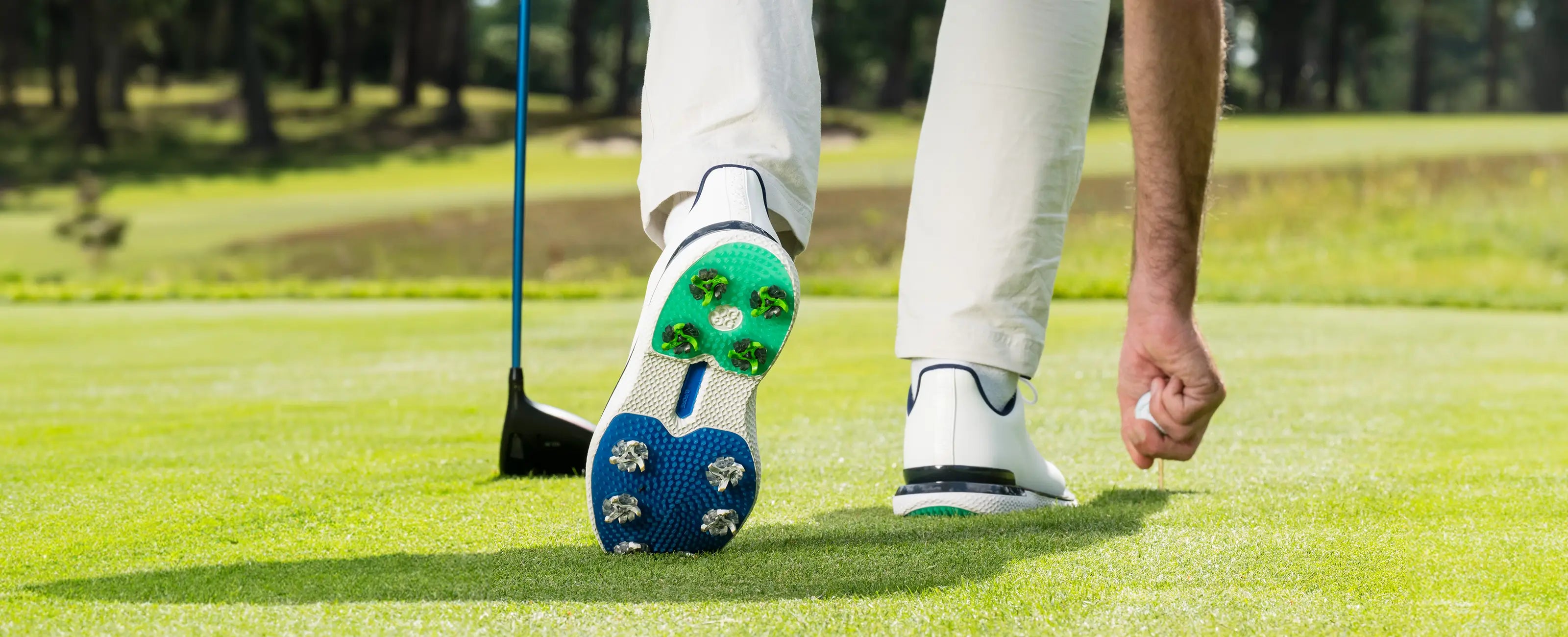 A person reaching for a golf tee with the bottom of their golf shoe exposed showing the attached Tour Flex Pro spikes. 