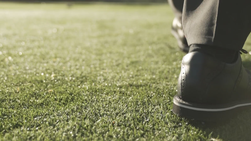 A close up of a golfers shoe walking on a green golf course. 