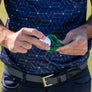 A person is placing a golf ball into a golf ball alignment tool while wearing a patterned shirt.
