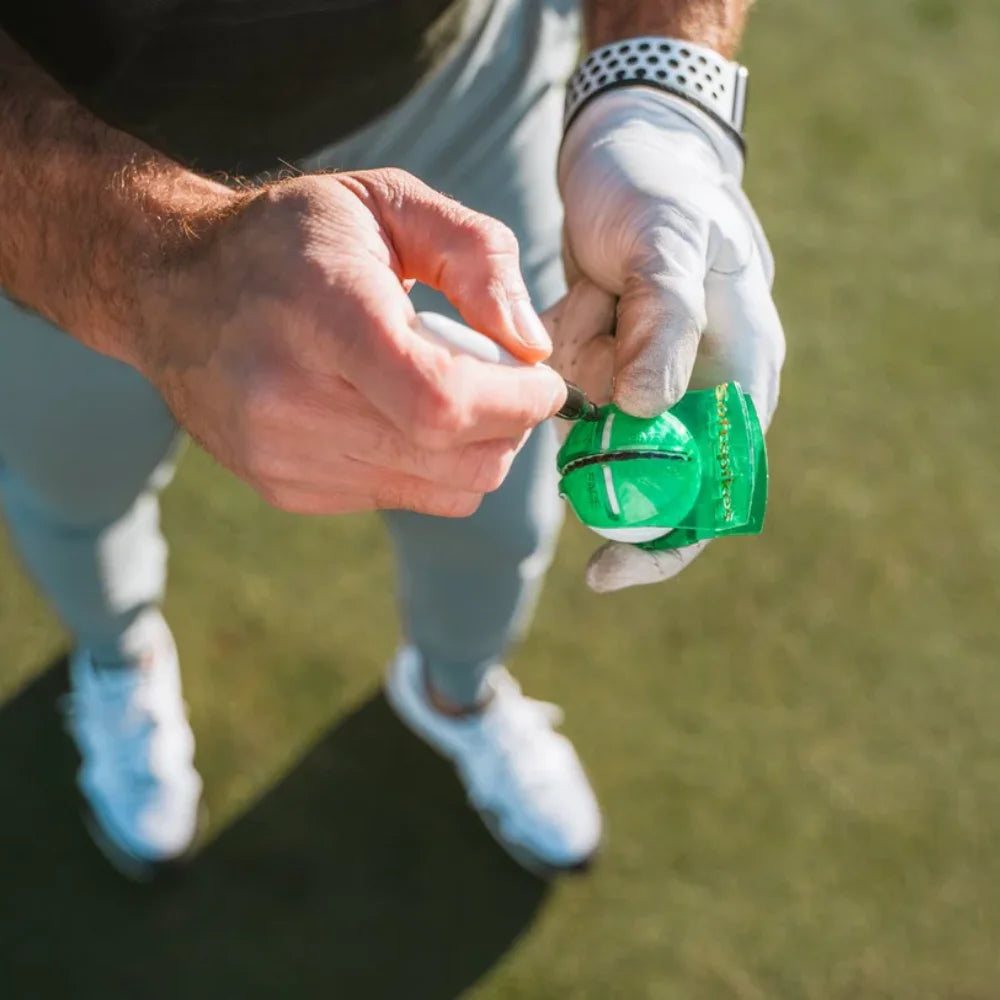 Person applying alignment details to a golf ball on a grassy background